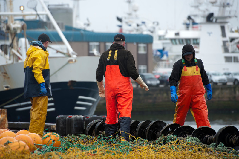 Photo of people working with a net on a pier in front of a fishing boat