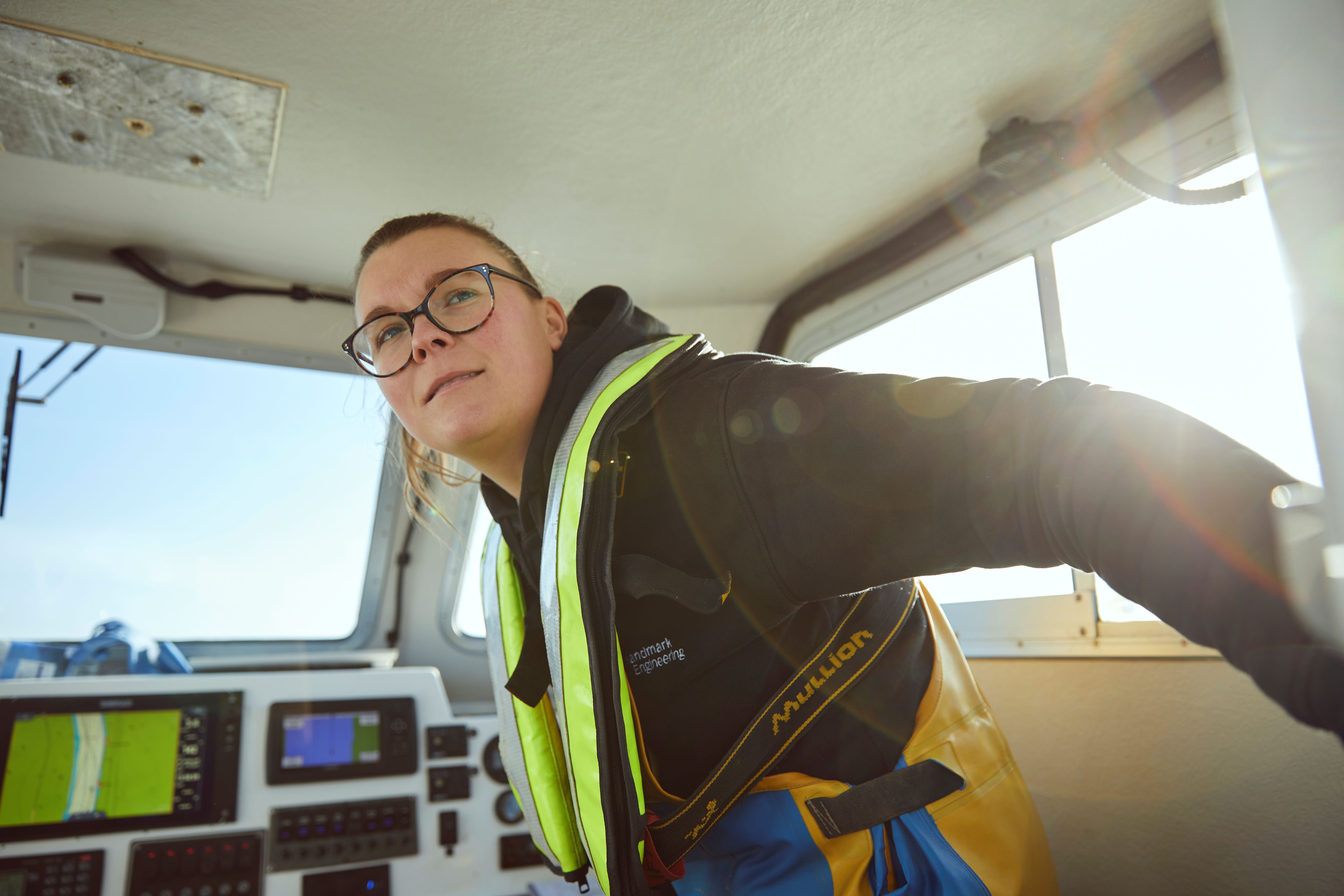 Photo of a woman in fishing gear and lifejacket in the wheelhouse of a boat