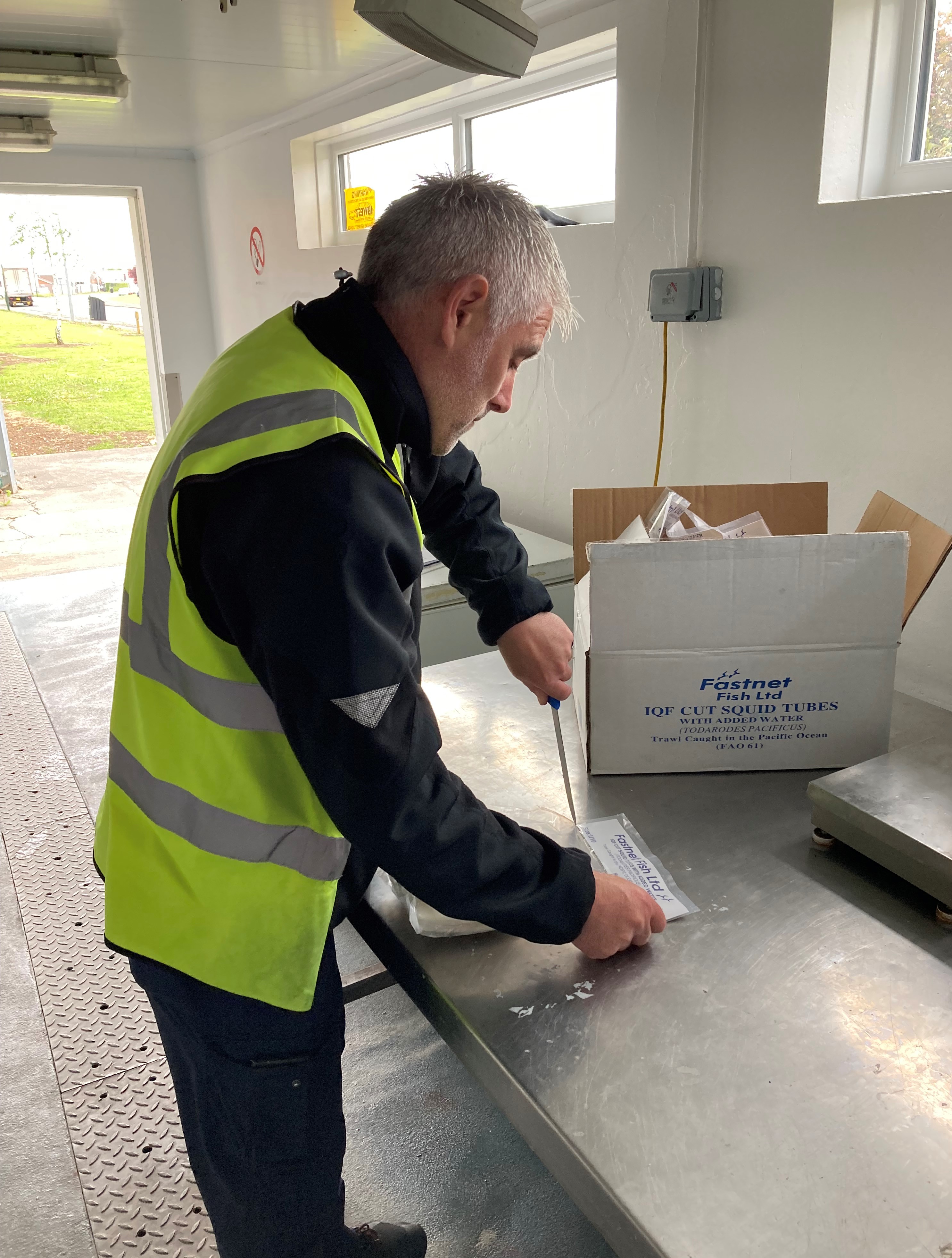 Man using a knife to slice open a plastic package containing cut squid tubes