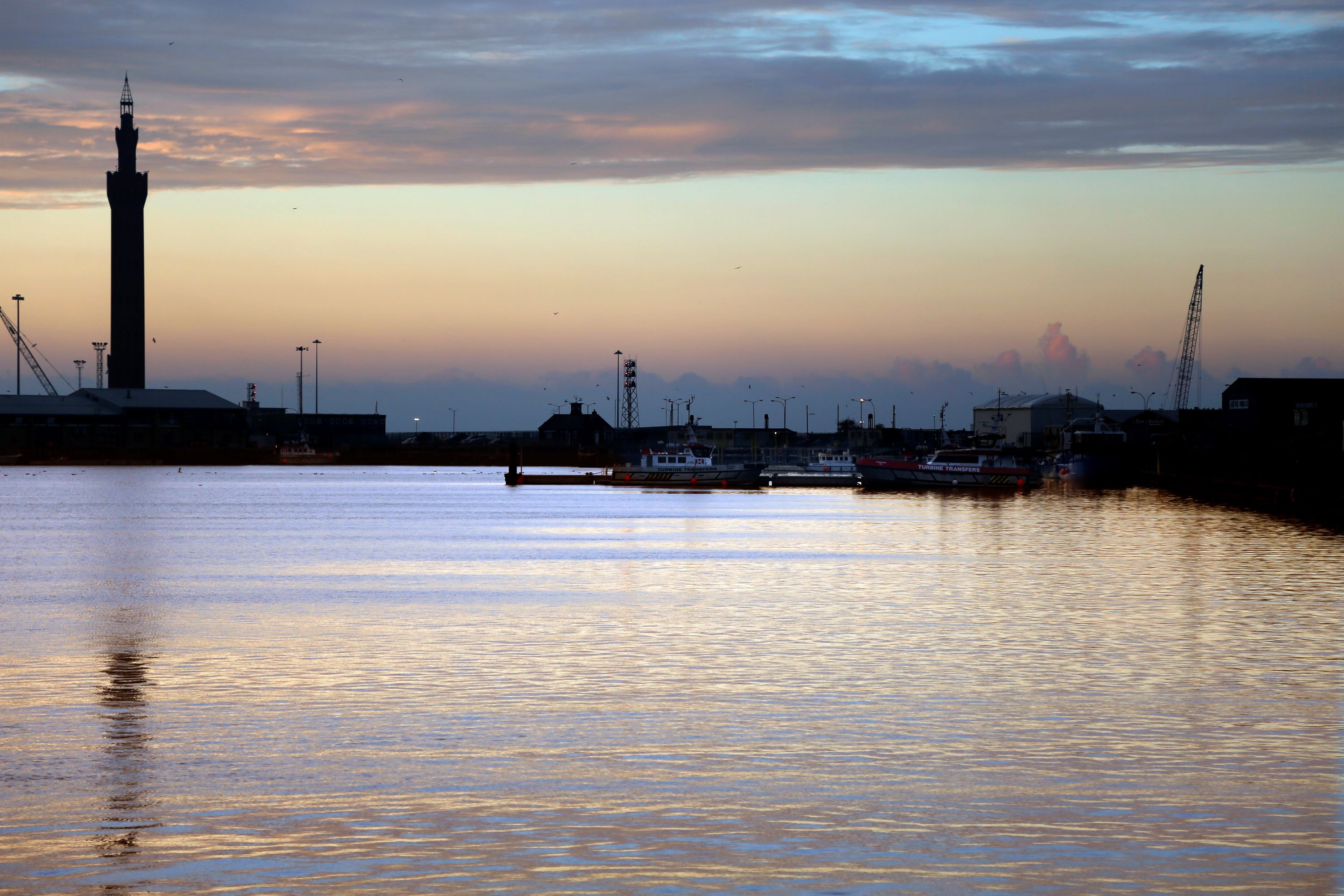 Dock at sunset with warm light reflecting onto the sea and several boats in the distance.
